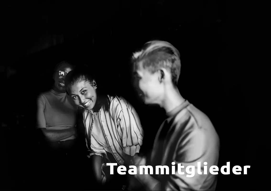 Drei Teammitglieder sitzen lachend zusammen, eine junge Frau schaut direkt in die Kamera